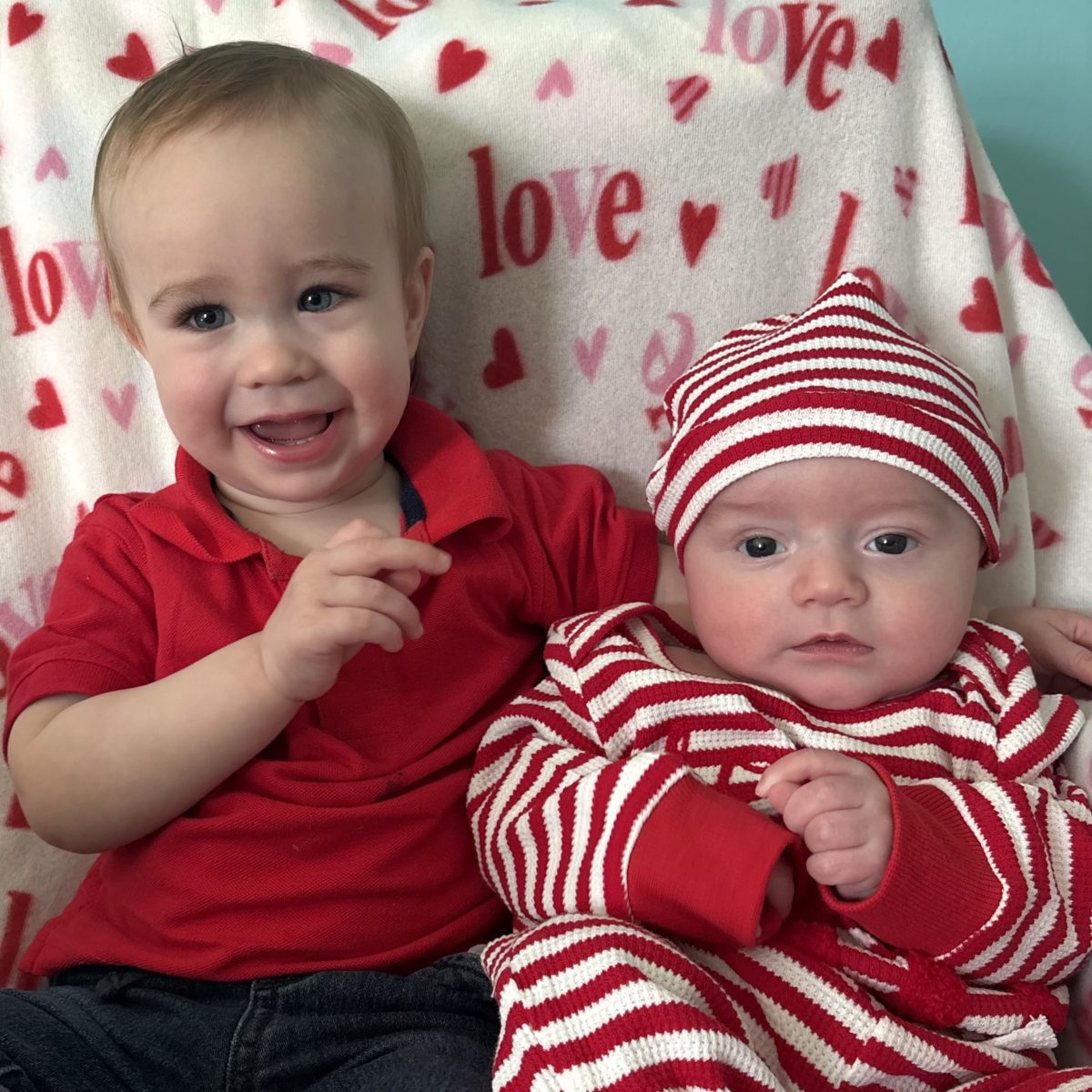 Two infants dressed in red and festive striped outfits sitting together during Spirit Week dress‑up day at The Clubhouse childcare center.